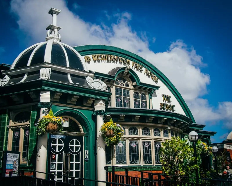 The Sedge Lynn in Chorlton, Manchester, a JD Wetherspoon pub in a former Temperance Billiard Hall, with a green and cream tiled front, a black and white dome and hanging baskets.