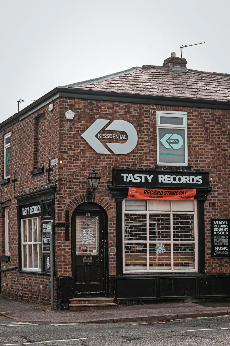 Tasty Records in Altrincham, a red brick corner shop with its name over the window, a Record Store Day banner and a board offering vinyl records bought and sold.